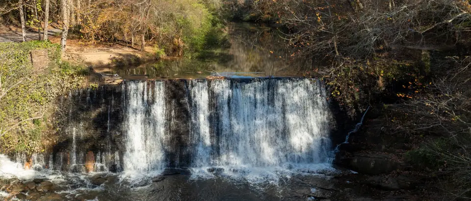 Water falling over the old stone mill dam on Vickery Creek in Roswell, Georgia, with autumn trees along both banks